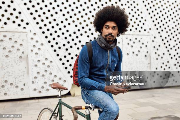 relajado hombre afrocaribeño con bicicleta que comprueba el teléfono inteligente - bigote manillar fotografías e imágenes de stock