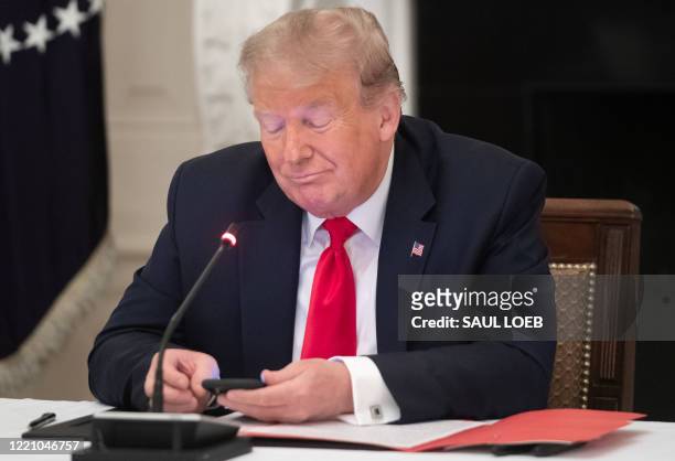President Donald Trump uses his cellphone as he holds a roundtable discussion with Governors about the economic reopening of closures due to...