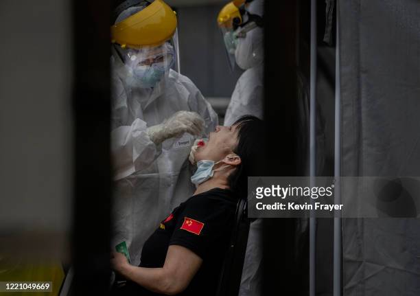 Chinese epidemic control worker wears a protective suit and mask while performing a nucleic acid test for COVID-19 on a woman who has had contact...
