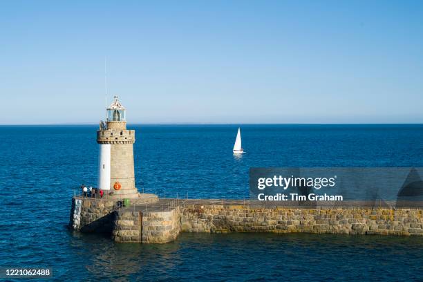 Yacht sailing past Guernsey island lighthouse and breakwater pier, St Peter Port, Channel Isles.