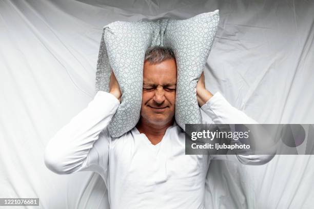 reifer mann fühlt sich unwohl im bett - hands covering ears stock-fotos und bilder