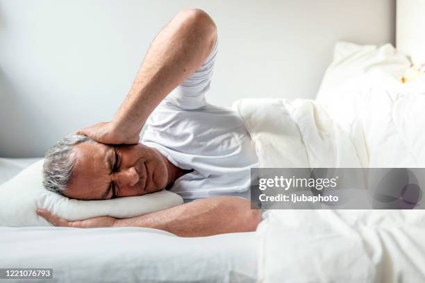 thoughtful man trying to sleep in his bed - hands covering ears stock pictures, royalty-free photos & images