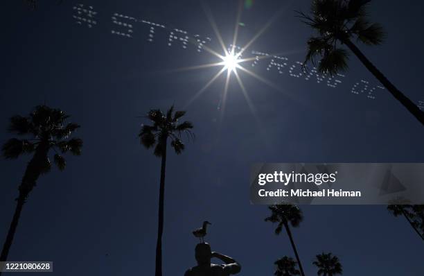 Seagull sits atop the Ben Carlson Memorial Statue as skywriting reading # Stay Stong OC is seen behind it on April 25, 2020 in Newport Beach,...