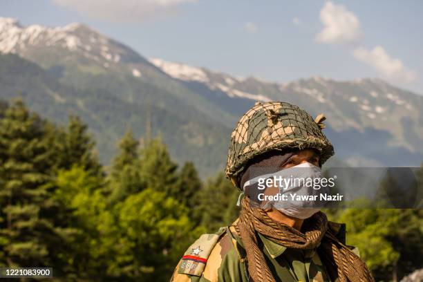 An Indian Border Security Force soldier wearing a mask guards a highway as Indian army convoy makes way towards Leh, bordering China, on June 19,...