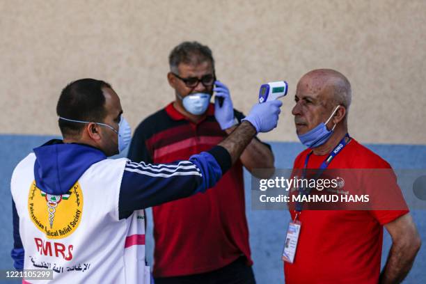 Palestinian medical worker checks the temperature of a member of the match-day staff football match behind closed doors between Shabab Rafah and...