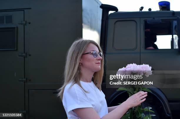 Woman walks with a bouquet of peony flowers past a police van during a gathering of opposition supporters to support candidates seeking to challenge...