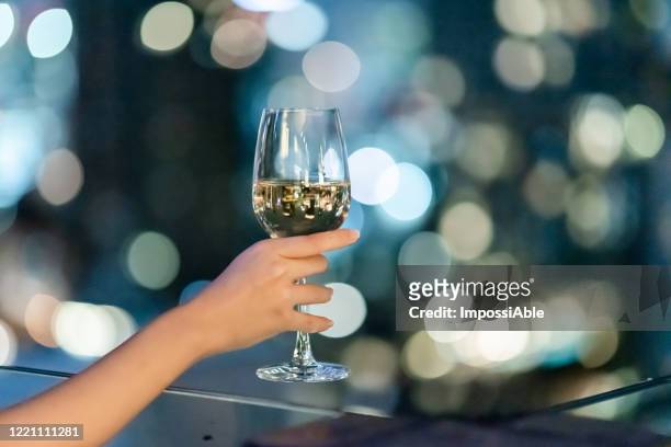 close up view of white wine glass at the rooftop bar with blur bokeh lights at night - champagne rooftop stock pictures, royalty-free photos & images