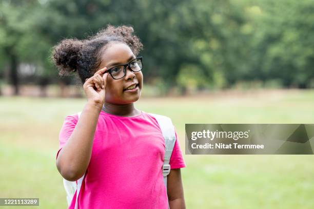 cute afro girl with curly hair, pigtail and eyeglasses looking away with a contented emotion while wearing casual clothing and backpack. - chubby girls photos fotografías e imágenes de stock