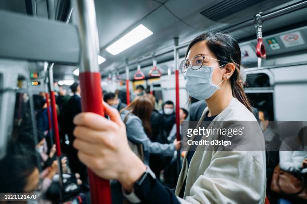 young asian businesswoman with protective face mask holding hand rail commuting in the city riding on a crowded subway in rush hour during the outbreak of covid-19 health crisis - state of emergency stock pictures, royalty-free photos & images