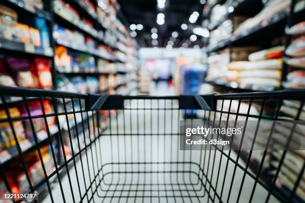 personal perspective of a shopper pushing shopping trolley along product aisle while shopping in a supermarket - supermarket shelves stock-fotos und bilder