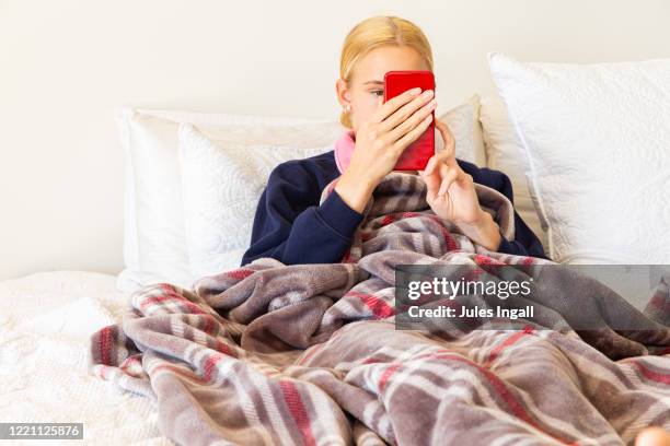 a young girl laying on her bed wrapped in a blanket face timing a friend - the face of australia photo call stock-fotos und bilder