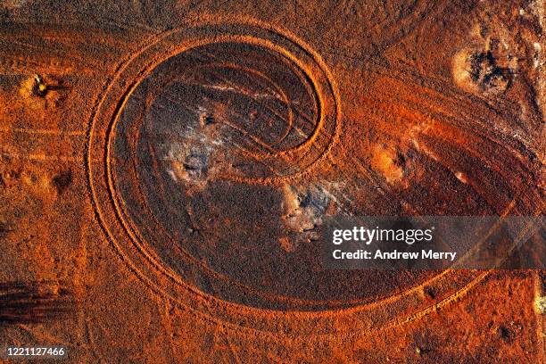 abstract swirl pattern from car tyre tracks in red dirt, illuminated by dusk sunlight, remote rural australia - red dirt stock pictures, royalty-free photos & images