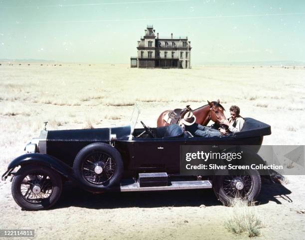 James Dean , US actor, on sitting in the backseat of a vintage motor car stroking a horse which stands beside the vehicle, a large house stands...