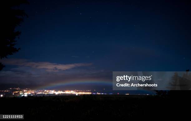 a moonbow over a dark field with city lights - moonbow 個照片及圖片檔