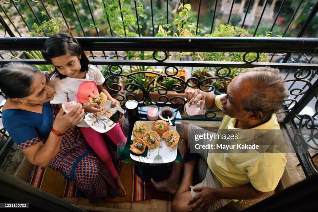 Senior couple enjoying snacks in the balcony with granddaughter