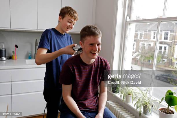 A young man having his hair cut at home by a teenage boy.