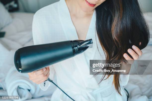 portrait of young asian woman using hair dryer for blows hot air to speed the evaporation of water to dry the hair in her bedroom. - dry hair photos et images de collection