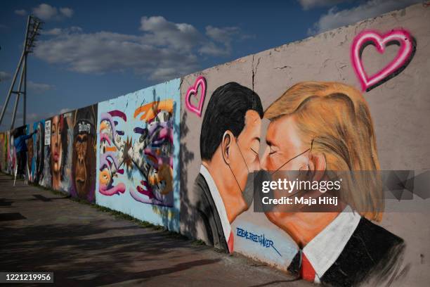 Street art shows US President Donald Trump and Chinese President Xi Jinping wearing protective mask and kissing at a section of the former Berlin...