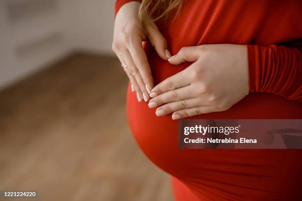 a pregnant woman in a red dress holds her pregnant belly with her hands. - red dress child stock pictures, royalty-free photos & images