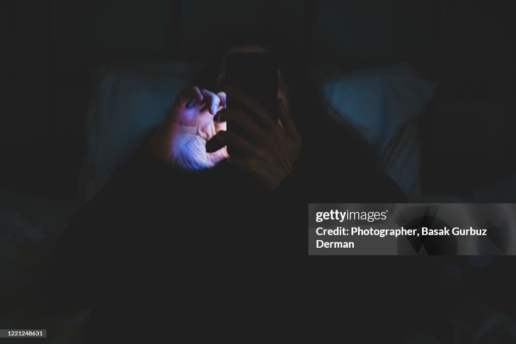 A woman using mobile phone in bed at night