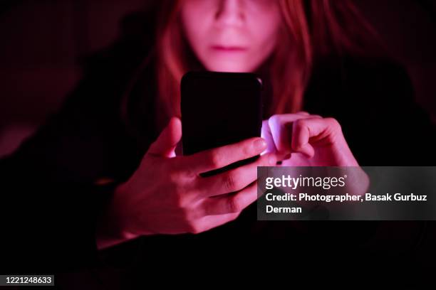 a woman using mobile phone at night, under colorful led lights at a pub / bar - dating stock-fotos und bilder