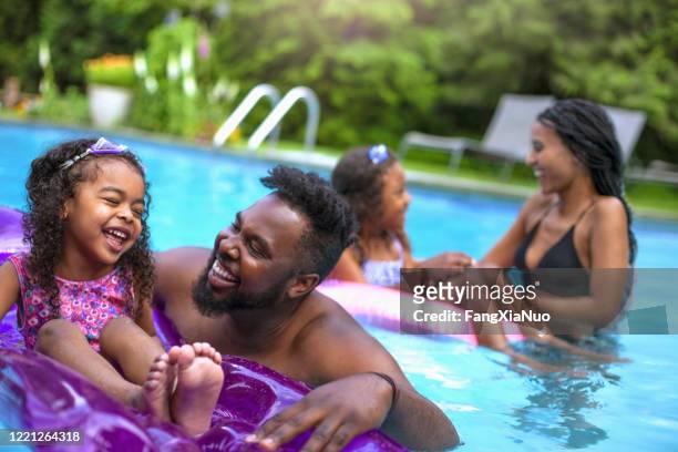 nette afroamerikanische familie mit zwei töchtern schwimmen im hinterhof pool - family pool stock-fotos und bilder