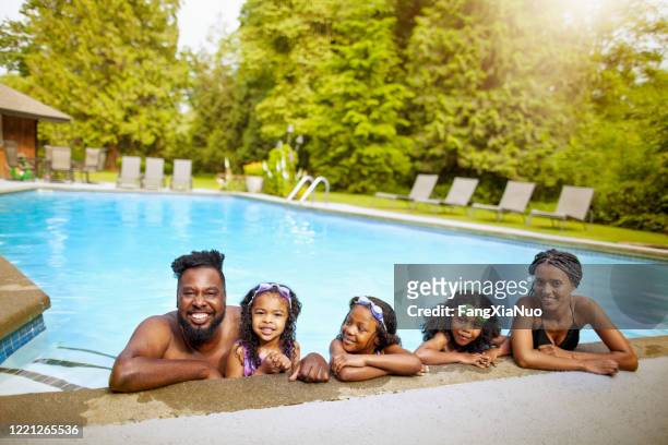 porträt einer afroamerikanischen familie mit drei kindern, die sich im hinterhof-wasserpool entspannen - family playing in backyard pool stock-fotos und bilder