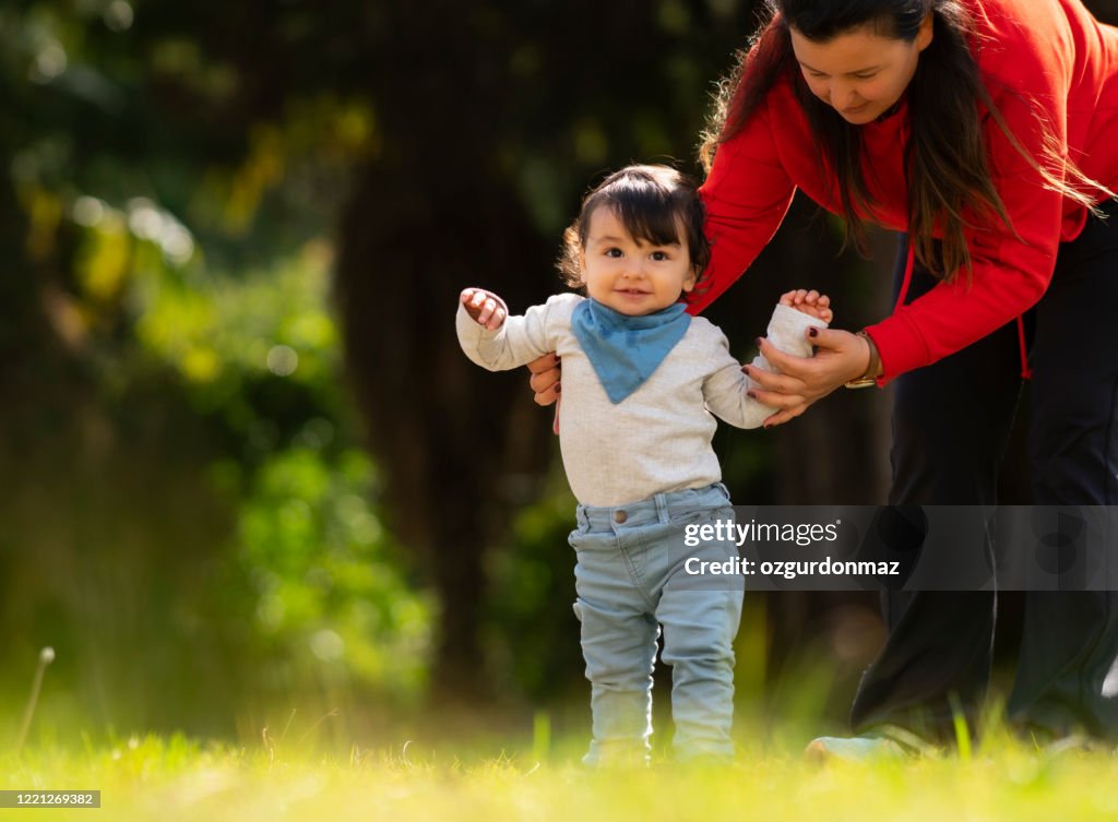 Mother helping baby boy to practice walking at the backyard