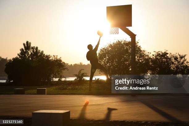 Teenager drives to the basketball hoop on a public court near the river Rhine at sunset during the novel coronavirus crisis on April 26, 2020 in...