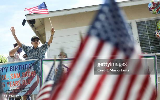 Army World War II veteran Lt. Colonel Sam Sachs, who turned 105 today, holds an American flag at his drive-by birthday party amid the coronavirus...