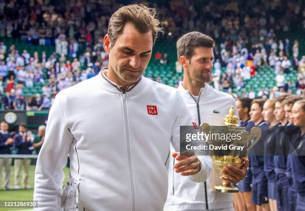 Roger Federer of Switzerland and Novak Djokovic of Serbia hold their trophies as they walk off Centre Court after the Men's Singles Final during the...