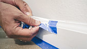 Removing masking tape from moulding. A painter pulls of blue painter's tape from the wall to reveal a clean edge baseboard.