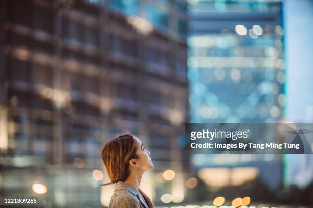 portrait of asian woman looking up to sky with confidence against illuminated city buildings at dawn - solo una donna giovane foto e immagini stock
