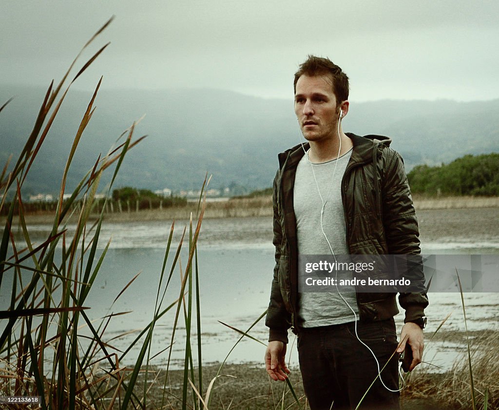 Young man listening song near lake