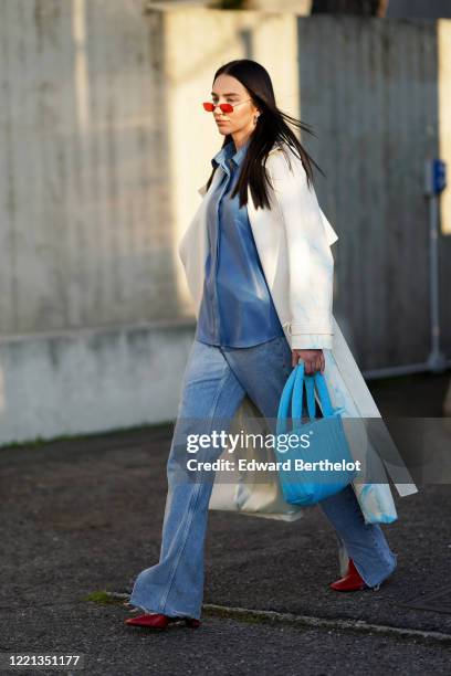Guest wears sunglasses, a white coat, a blue jacket, blue denim flared ripped jeans, a blue bag, red pointy shoes, outside Alberta Ferretti, during...