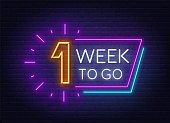 One week to go neon sign on brick wall background.