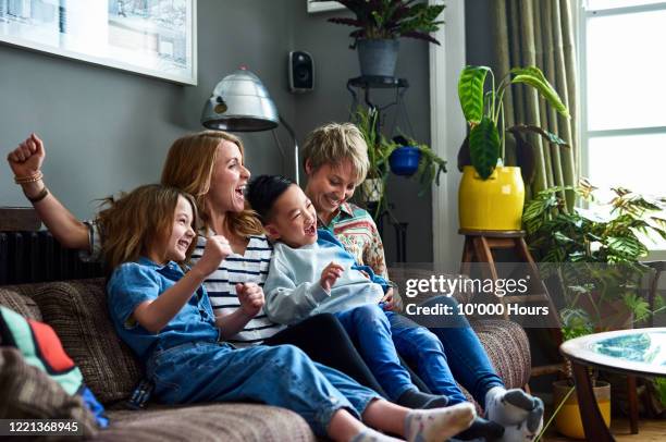 cheerful family with two mums watching tv at home - adopted chinese daughter ストックフォトと画像