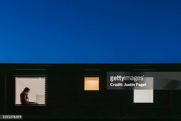night time view of home exterior - figure on laptop in the window - quarantäne stock-fotos und bilder