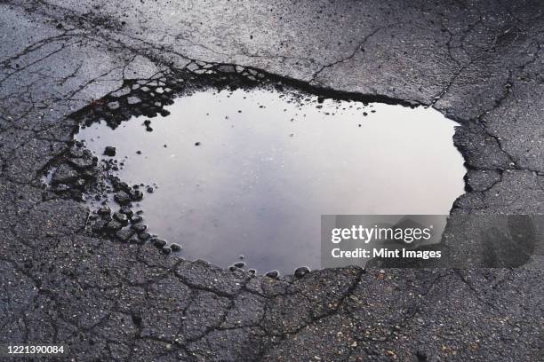 water filled pothole on urban street with cracks and fracture marks - pothole photos et images de collection