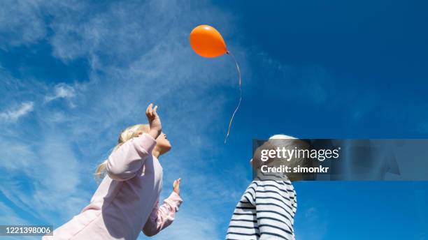 niños liberando globo en el cielo azul - balloon girl fotografías e imágenes de stock