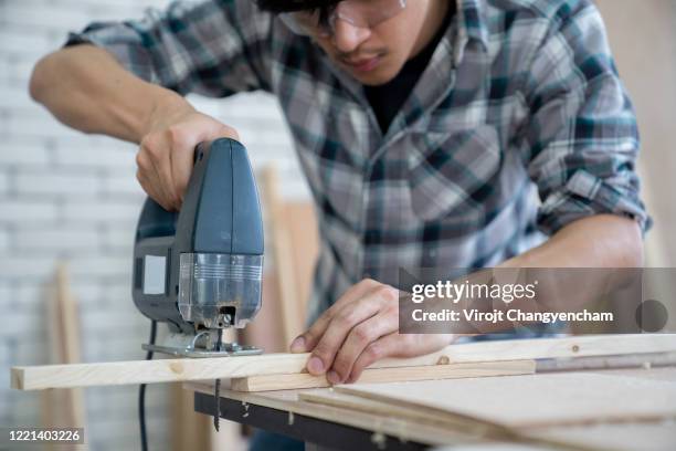 young carpenter working sawing wood by electric jigsaw. - serra tico tico serra elétrica - fotografias e filmes do acervo