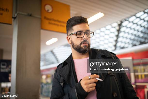 man smoking cigarette while waiting for a train at railroad station - railroad station platform stock pictures, royalty-free photos & images