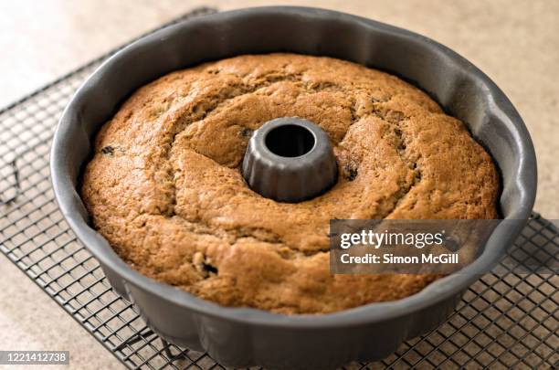 freshly baked homemade rum and raisin bundt cake on a cooling rack in its cake tin - tulbandcake stockfoto's en -beelden