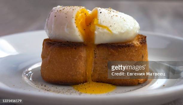 poached egg, liquid yolk with, green onion on toast bread, white plate on white wooden background - pochiert stock-fotos und bilder