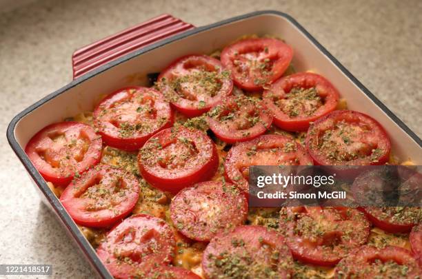 cheesy pasta bake topped with sliced tomato and dried oregano ready for baking - origano foto e immagini stock