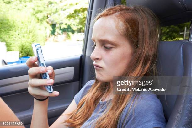 young redheaded girl brown eyes and freckles sitting in passenger seat using cellphone not looking at the camera feet up on the dashboard typing on phone close up putng and scrunching face together