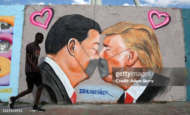 Pedestrian passes graffiti of Communist Party of China General Secretary Xi Jinping and U.S. President Donald Trump kissing each other while wearing...