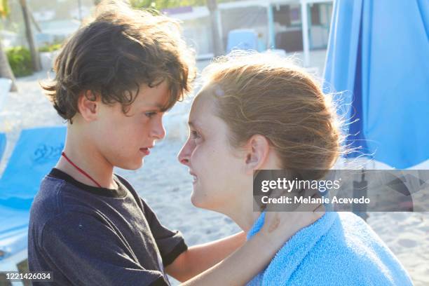 Close up shot of a little boy with brown curly hair nose to nose with his big sister who has red hair, and is laughing. She is aprox 12 yrs old and he is aprox 6yrs old. They are outside on a beach together, in beautiful light.