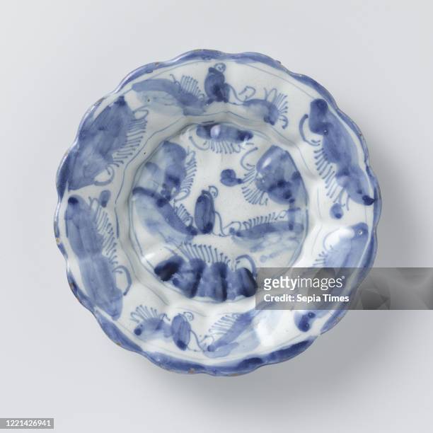 Plate, Round plate of blue painted faience, with a ribbed and scalloped edge. A seated figure in a landscape is painted on the shelf and two seated...