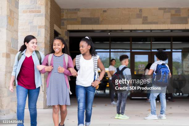 after school, three friends exit arm in arm - arm in arm stock pictures, royalty-free photos & images